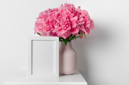 Blank white photo frame mockup with big pink peony flowers bouquet, copy spaceの写真素材