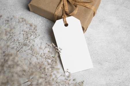 Gift box with blank tag and dried flowers on grey background, white tag card with copy space