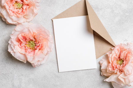 White invitation card with envelope on gray conxrete background with fresh roses flowers. Blank card...