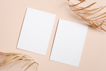 Two blank vertical white cards on a soft beige surface, decorated with dried palm leaves, ideal for...