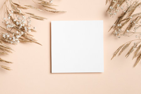 Blank square paper card mockup with copy space on beige background with dried grass and gypsophila flowers decor, perfect for wedding invitations or greeting cardsの写真素材