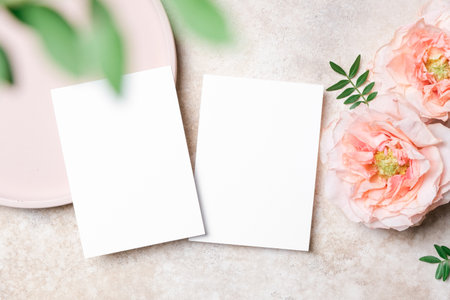 Two vertical white blank wedding invitation cards on a textured background with roses flowers and green leaves. Elegant flat lay, perfect for invitations or greeting card designsの写真素材