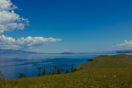 In the foreground is part of the green cape. In the distance a blue water surface. Blue sky, clouds. Summer sunny day. Nobody here.の写真素材
