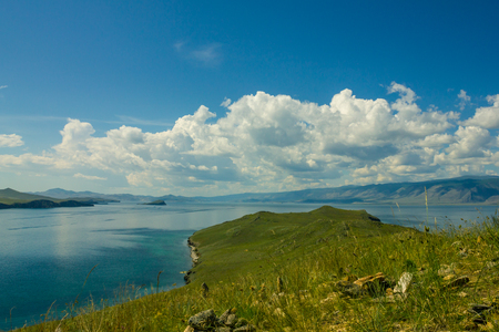 In the foreground is part of the green cape. In the distance a blue water surface. Blue sky, clouds. Summer sunny day. Nobody here.の写真素材