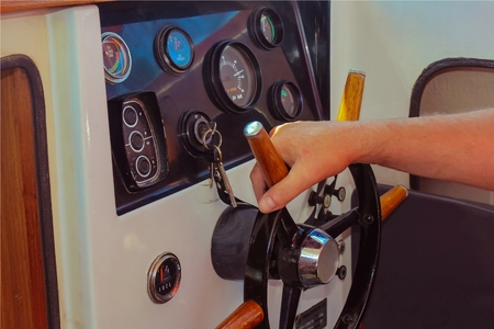 Helmsman. The man's hand holds the steering wheel steadily. Close-up of the handle of the wheel and dashboard. Keys in the ignition lock. The helmsman manages the ship.の写真素材