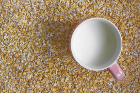 On a yellow background of oatmeal flakes is a pink mug with white milk. Proper nutrition, diet,...