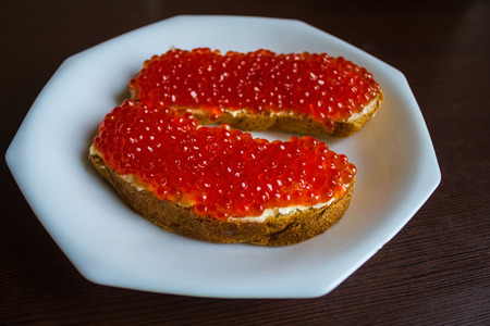 On a white dish, two sandwiches with salmon caviar. Rough bread, butter and shiny large eggs. An...