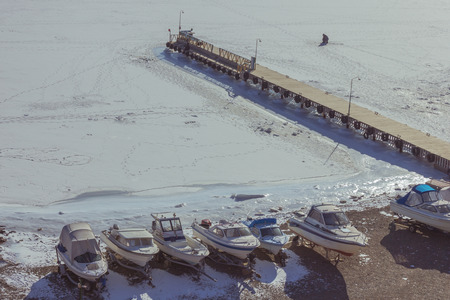 Boats on a frozen seashore, in the distance pier. On the ice track tracks. Around the snow. Boat...