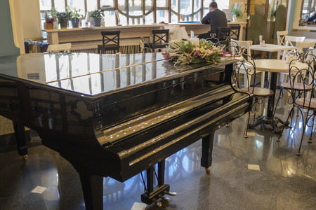 An old cafe with vintage furniture and a black grand piano. A man sitting by the window looks at the street. Loneliness, expectation, sadness.の写真素材