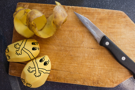 On an old wooden board a knife and raw potatoes, near cleaning. Work in the kitchen, cooking. Top view, daylight. The picture is made by the author.の写真素材