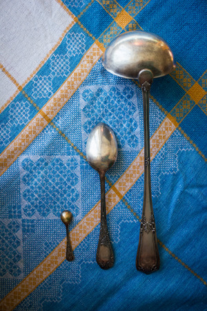 Ancient silver spoons of different sizes. Household, kitchen, dining utensils. A blue linen tablecloth. View from above.の写真素材