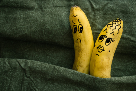 Passionate, sexy woman and a sluggish, cold man. Two bananas on dark sheets, a metaphor. Husband and wife, lovers. The picture is made by the author.の写真素材