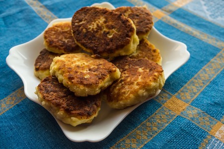 The dining table is covered with a blue tablecloth. On a white plate homemade cakes, yellow pancakes. Simple delicious food, handmade. Daylight.の写真素材