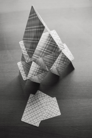 An easily broken, unreliable, temporary home made of playing cards. Empty calculation, futile effort. Black and white, side lighting.の写真素材