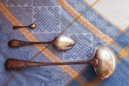 On the blue tablecloth are three different silver spoons. Women of different ages in the same family. House utensils, work in the kitchen, cooking. Daylight, top view.の写真素材