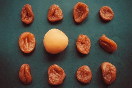 A beautiful, fresh apricot is surrounded by withered, wrinkled fruits. Beautiful appearance, youth, good skin. Top view, dark background, toning.の写真素材