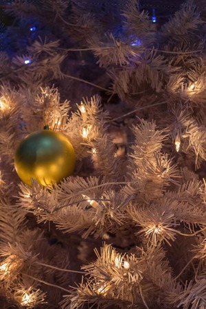 Backlight, twinkling lights and a large ball on the white branches of the Christmas tree. Waiting for the holiday, New Year's Eve. Vertical arrangement, toning.の写真素材