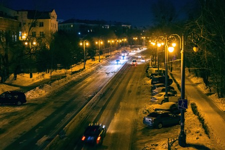 The winter road is illuminated by street lights. Modern city, winter, evening. Naked trees, buildings, snow. View from above.の写真素材