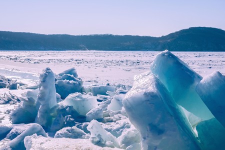 Snow, ice, frozen river, bay. Ice hummocks in the foreground. Away the horizon, the hills. Lateral solar illumination. Blue toning.の写真素材