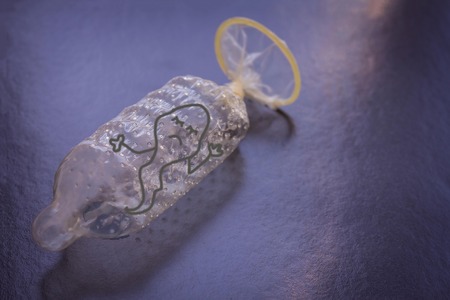 The condom is securely tied in a knot. Inside the sad sperm can not go outside. Dark background, blue toning. Copy space. Figure made by the author.の写真素材