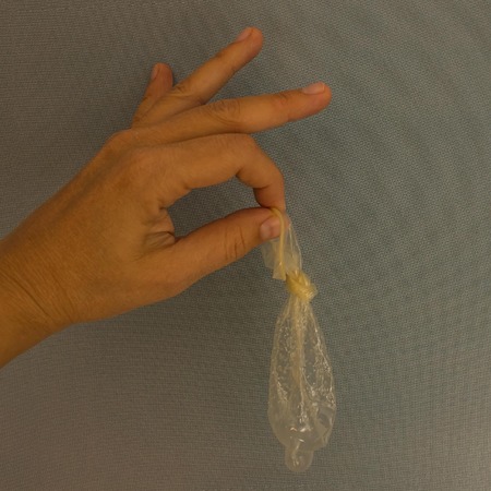 Hand holding a condom. Lack of consequences, control over the situation, guarantee of reliability, contraception. Gray background, daylight.の写真素材