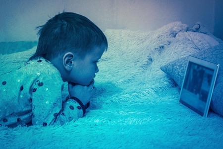 Computer addiction, harm of gadgets, children's leisure. A little boy in the bedroom is watching a...