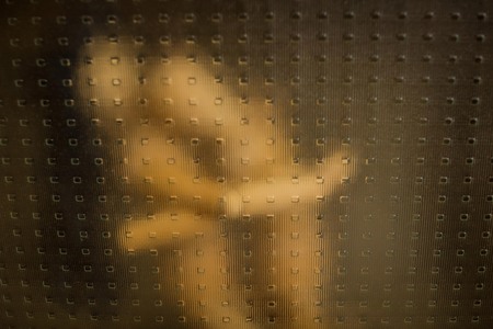 Cuddling lovers, nudes. A man caresses a woman, petting. Looking through the glass, everything is blurry. Copy space.の写真素材