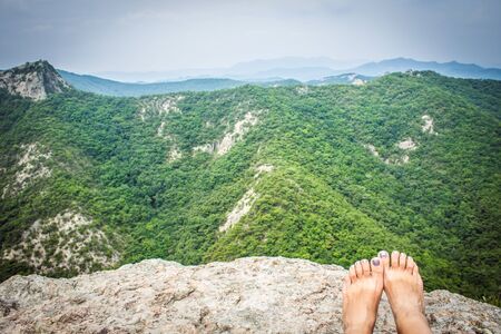 Beautiful mountain landscape, green and blue colors, summer. In the foreground are the female feet. Solo travel.の写真素材