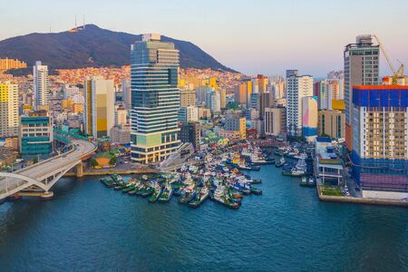 Modern city at sunset, yellow tones. Tall buildings, bridge. There are many fishing vessels in the...