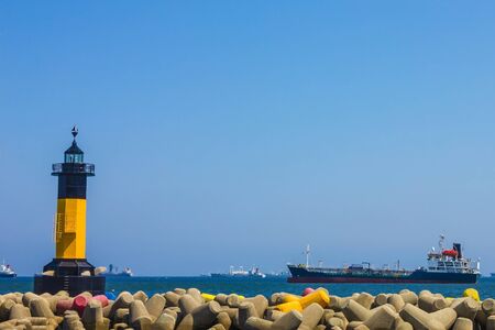 Sea harbor bay. Yellow lighthouse. Far ships, skyline. Bright sunny day, blue sky.