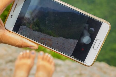 A girl photographs green mountains. Summer day, the top of the cliff. Vacation, freedom.の写真素材