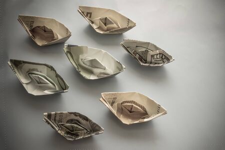 Paper ships on a gray background. Euro and dollars.  Ships idle, financial loss. Vignetting, top view.の写真素材