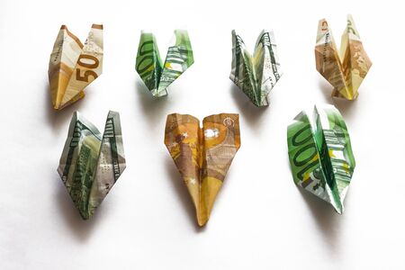 Paper airplanes, banknotes of different colors, euros and dollars. Airlines, passenger transportation. Flight transfer. Light background.の写真素材