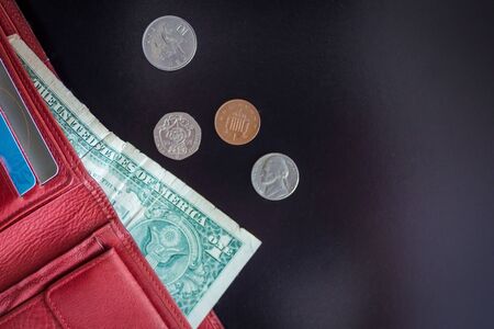 From the red open purse sticks out one dollar, next to a few small coins. Budget calculation, increase in costs, the financial crisis. Dark background.の写真素材