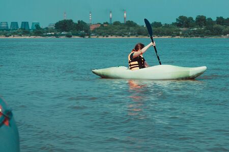 Rest in the city, an active lifestyle. A girl in a kayak swims along the shore of an industrial...