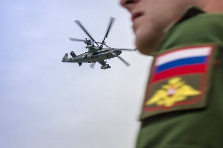 Military helicopter in the sky, aviation. In the foreground is the figure of an officer in Russian military uniform. Teachings, maneuvers. The foreground is blurred.の写真素材