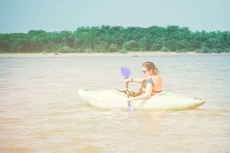 Kayaking, water recreation. A girl in a life jacket on a kayak, in the hands of a paddle. Lake, river, sea. Active lifestyle. Bright sunny lighting, tinting.の写真素材