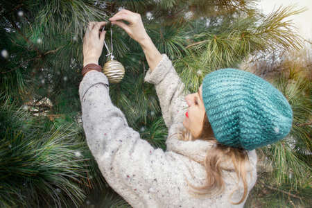 Decorating a Christmas tree with New Year's toys. Waiting for the holiday, preparation. Live green spruce in the yard of the house.の写真素材