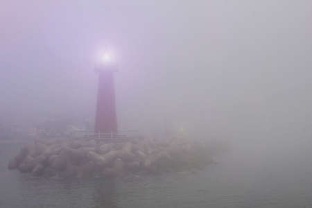 Red lighthouse at the entrance to the bay. Thick fog, nothing is visible. Around the dark water.の写真素材