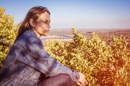 Youth, travel, freedom, lifestyle. The girl with long hair looks into the distance. Sky, green landscape. Muffled tones, copy space.の写真素材