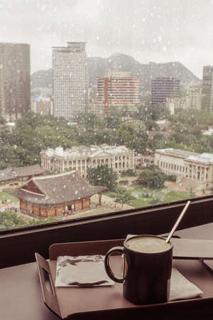 The view from the window on the old center of Seoul. Royal Palace and modern buildings. Early autumn, snow, rain. In the foreground is hot coffee. Loneliness, sadness, melancholy.の写真素材