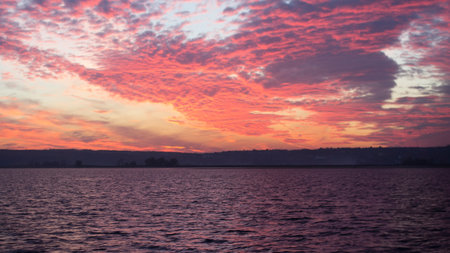 Colorful sunset over the sea, river, lake. Red, crimson, purple and orange clouds. In the distance the coastline, the horizon line.の写真素材