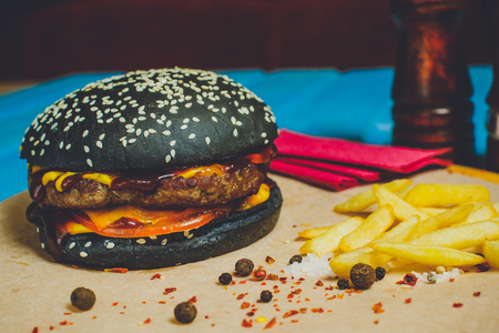 Fresh beef burger with cheese, vegetables and spicy tomato sauce on paper, blue wooden backgroundの写真素材