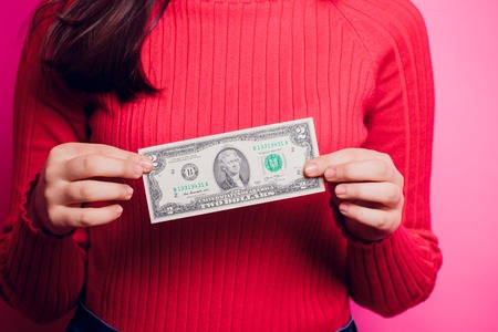 Hand holding two dollar bill. Isolated on a colored sweater.の写真素材