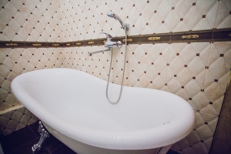 Modern bathroom with a shower area and bath tub including a wall mirror beside a fancy plant near a tap and sink over the wooden counter and dark cupboardの写真素材