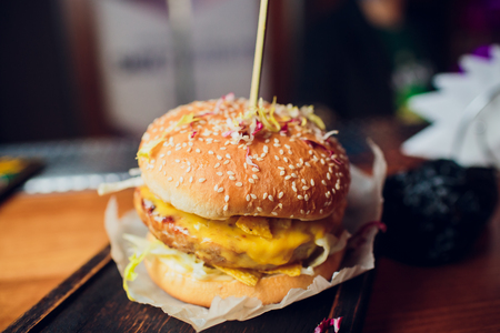 Tasty grilled delicious burger with lettuce, cheese, onion and tomato on a rustic wooden plank on a dark brown background clubの写真素材