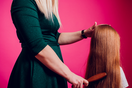 Mother combing daughter, care about hairstyle. Girl is unhappy mom pulling her hair. Important role in child life. Femaleの写真素材