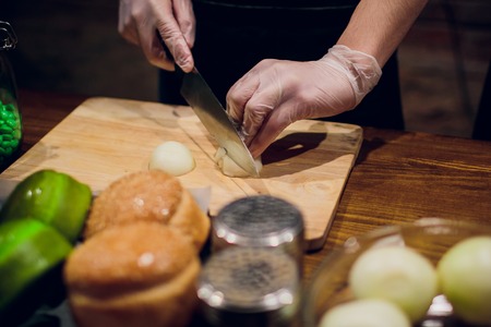 Chef's hands with knife cutting the onion on the wooden board. Preparation for cooking. Healthy eating and lifestyle. Male Manの写真素材