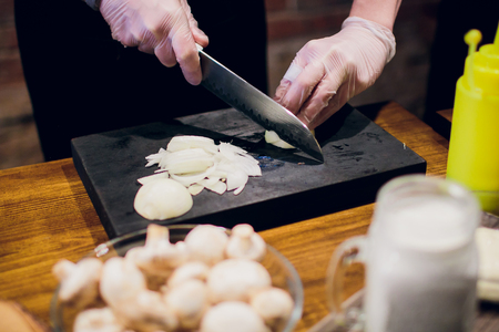 Chef's hands with knife cutting the onion on the wooden board. Preparation for cooking. Healthy eating and lifestyle. Male Manの写真素材