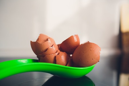 Flat lay above egg and eggshells on kitchen a green spoon on an electric black plate with natural light.の写真素材